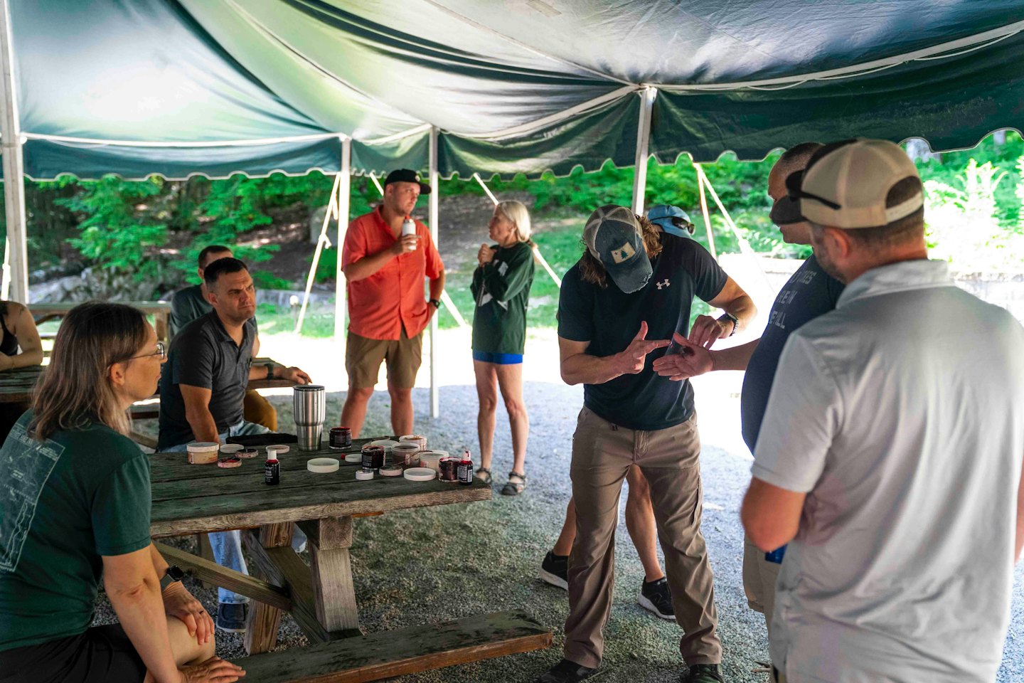 Een groep volwassenen luistert naar een workshopdocent onder een tent.